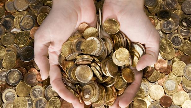 Zwei Hände halten eine Fülle von Euro-Münzen über einem Haufen weiterer Münzen.