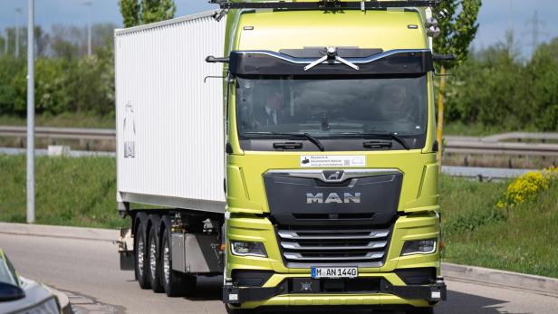 Ein gelber MAN-Lkw mit weißem Anhänger fährt auf einer Straße.