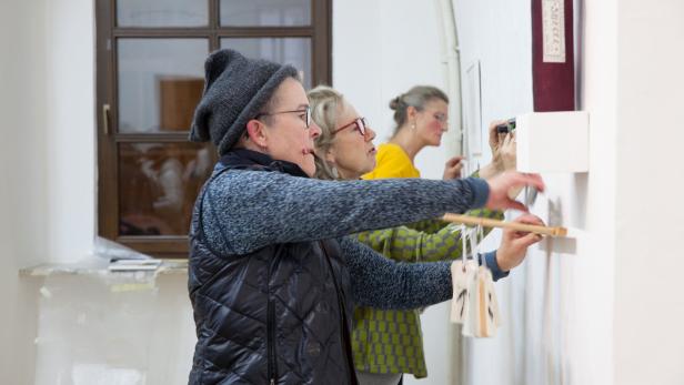 zwei Frauen befestigen Bilder an einer Wand