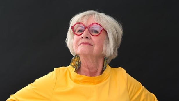 Frau im gelben Kleid und mit roter Hornbrille blickt in die Kamera