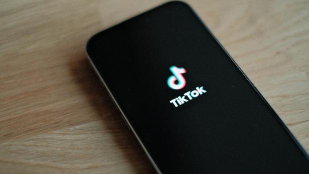 Handy mit TikTok-Logo liegt auf einem braunen Holztisch.