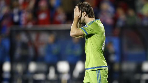 Ein Fußballspieler in grüner Uniform hält seine Hände vor das Gesicht.