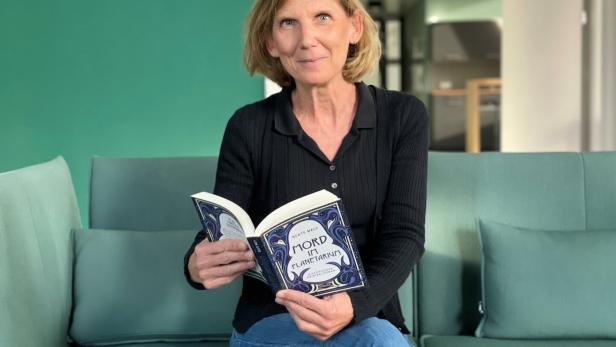 Beaty Maly sitzt auf einer Couch und blättert in ihrem neuen Buch