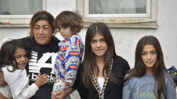 Eine Mutter mit ihren vier Kindern steht vor einer weißen Hauswand.