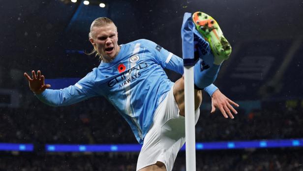 Ein Fußballspieler im blauen Trikot hebt das Bein hoch und berührt mit dem Fuß eine Eckfahne im Stadion.