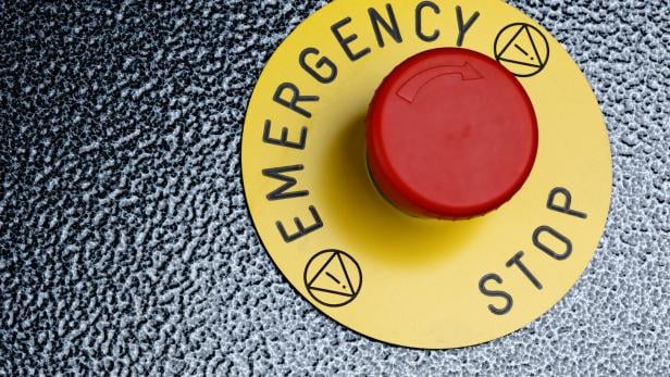 Ein roter Knopf auf einer gelben Plakette, auf der Emergency Stop steht.