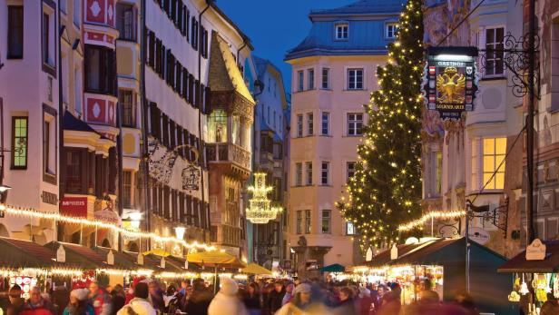 Ein belebter Weihnachtsmarkt in Innsbruck mit geschmücktem Baum und dem Gasthof Goldener Adler im Hintergrund.