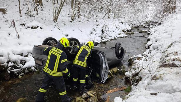 Zwei Feuerwehrleute bergen ein Auto, das kopfüber in einem verschneiten Bach liegt.