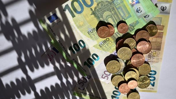 Mehrere Euro-Geldscheine und Münzen liegen auf einer weißen Fläche im Schatten eines Abakus.