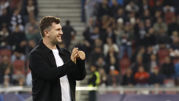 Ein lächelnder Mann in Jacke klatscht vor einer Zuschauermenge.