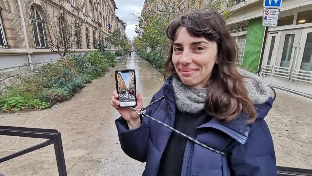 Eine Frau zeigt auf einem Handy, wie die Straße, in der sie steht, früher ausgesehen hat.