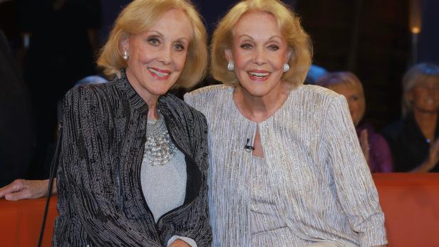 Die Kessler-Zwillinge lächeln in glitzernden Jacken nebeneinander.