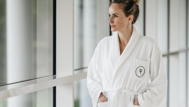 Eine Frau im Bademantel schaut aus dem Fenster.