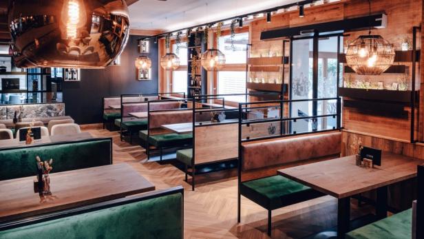 Innenansicht eines Restaurants mit Holzdecken und grünen Sitzbänken.
