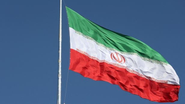 Die iranische Flagge weht vor blauem Himmel.