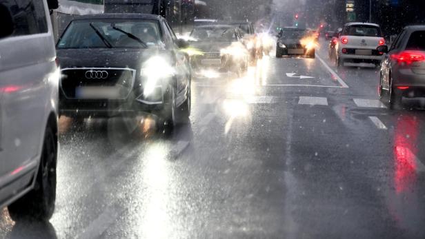 Mehrere Autos fahren bei Regen und schlechter Sicht mit eingeschaltetem Licht auf einer nassen Straße.