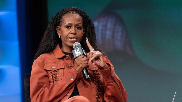 Michelle Obama mit Zöpfen spricht in ein Mikrofon mit dem SXSW-Logo und gestikuliert.