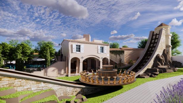 Eine runde Freizeitpark-Attraktion mit Sitzplätzen fährt vor einem mediterranen Gebäude und einer steilen Schienenrampe.