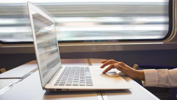 Eine Person arbeitet an einem Laptop auf einem Tisch in einem fahrenden Zug.