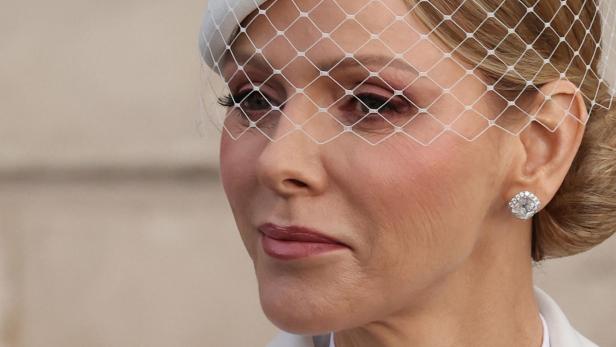 Charlene von Monaco mit blonden Haaren trägt einen weißen Hut mit Schleier und einen Diamantohrring.