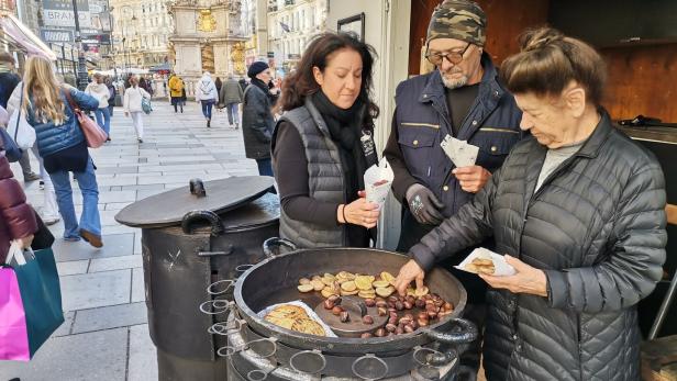Zwei Frauen und ein Mann bei einem Maroniofen.
