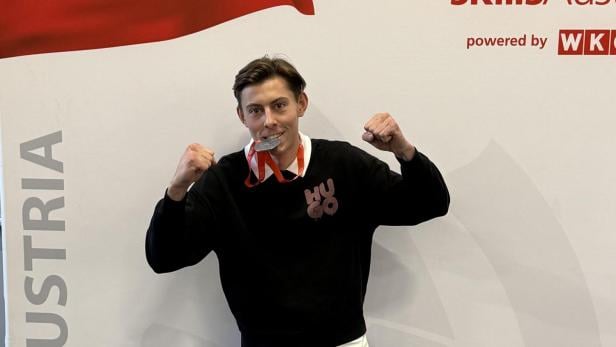 Junger Mann mit Silbermedaille vor SkillsAustria-Logo und österreichischer Flagge.