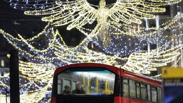 Ein roter Doppeldeckerbus fährt nachts unter leuchtender Weihnachtsdekoration in Engelsform entlang.