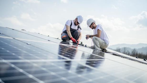 Team of two workers on a house's roof installing solar panels.