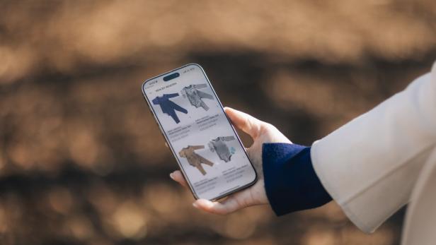 Eine Person hält ein Smartphone, auf dem verschiedene Babyanzüge in unterschiedlichen Farben angezeigt werden.