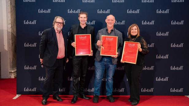 Vier Personen stehen auf rotem Teppich vor einer Wand mit „falstaff“-Schriftzug und halten gerahmte Auszeichnungen.