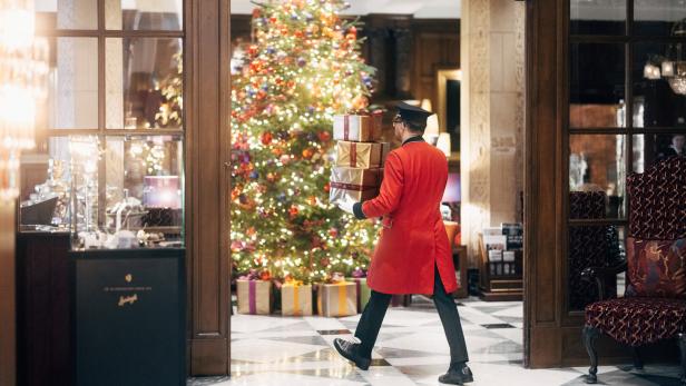 Ein Mann, der ein Geschenk in eine Hotellobby mit einem großen Christbaum trägt.
