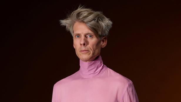 Ein blonder Mann in einem rosa Pulli