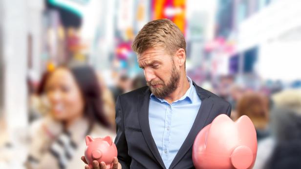 Mann im Anzug blickt besorgt auf zwei unterschiedlich große Sparschweine in den Händen.