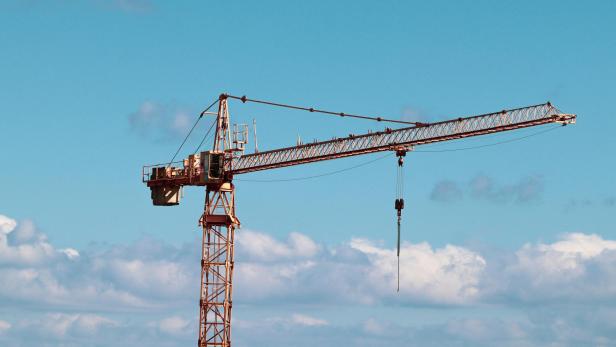 Ein Baukran ragt vor blauem Himmel und einigen Wolken empor.
