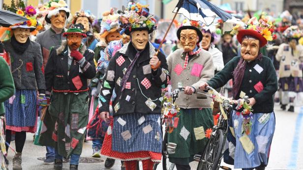 Eine Gruppe verkleideter Menschen mit Masken und bunten Kostümen zieht durch die Straße.