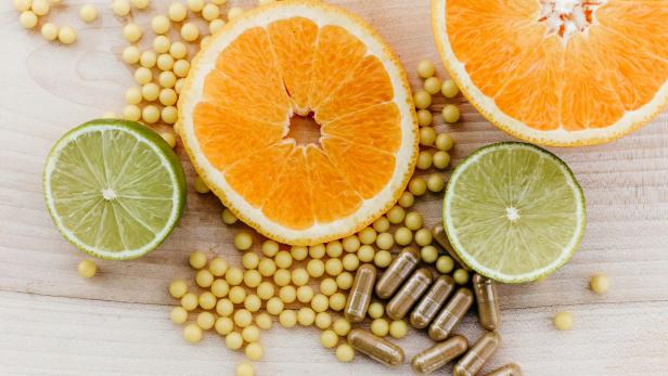 Halbierte Orangen und Limetten mit gelben Tabletten und braunen Kapseln auf Holzuntergrund.