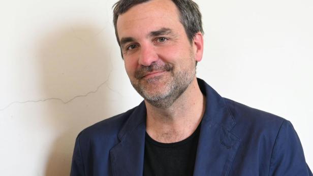 Florian Klenk in blauem Sakko lächelt vor einer hellen Wand.