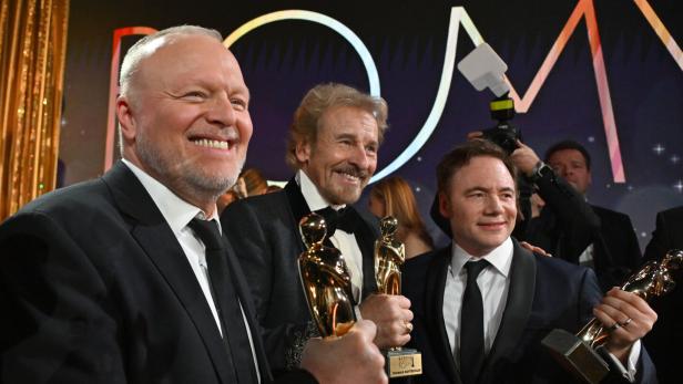 Raab, Gottschalk und Bully halten lächelnd goldene ROMY-Statuen in den Händen.