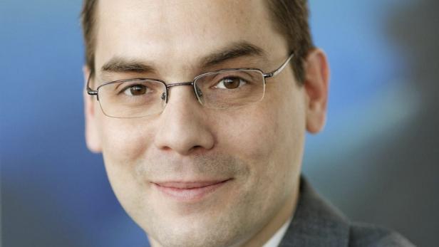 Ein Mann mit Brille und Anzug vor einem blauen Hintergrund.