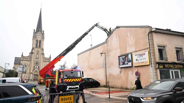 Eine Feuerwehrleiter ragt zu einem Gebäude, während Polizisten eine Straße vor einer Kirche absperren.