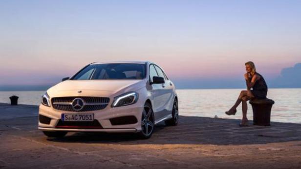 Ein weißer Mercedes-Benz steht an einem Kai, während eine Frau am Wasser sitzt.