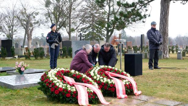 Mehrere Personen legen Kränze an Friedhof nieder