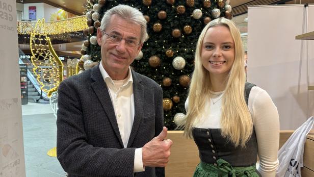 Ein Mann im Sakko und eine Frau im Dirndl posieren vor einem Weihnachtsbaum.