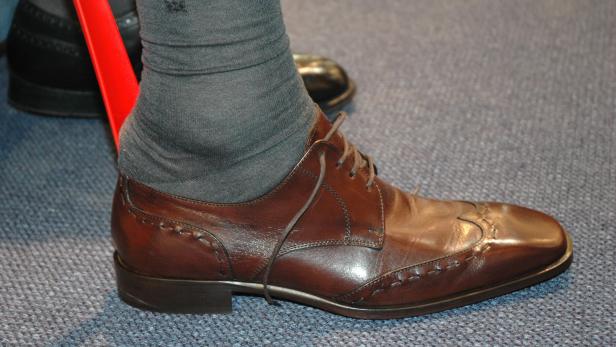 Ein oranger Schuhlöffel steckt in einem eleganten Lederschuh.