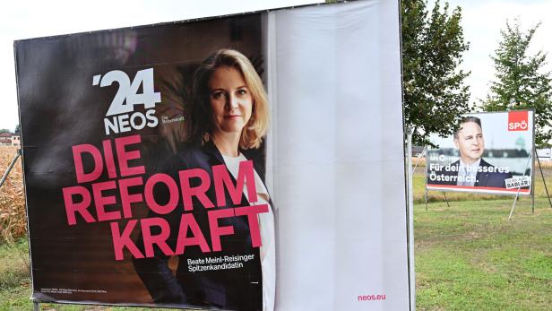Wahlplakate auf Wiese, Neos im Vordergrund, dahinter SPÖ
