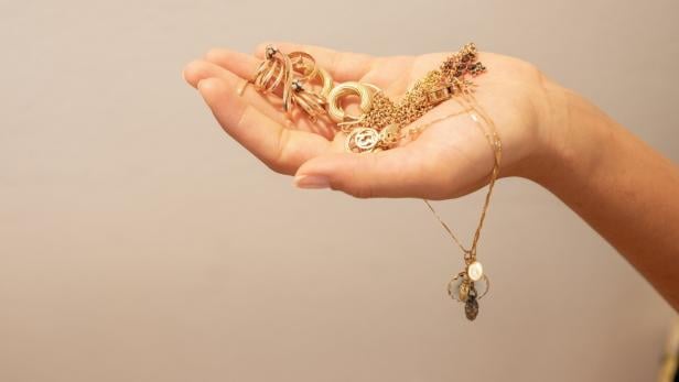 Eine Frauenhand hält einige goldene Schmuckstücke in der Hand.