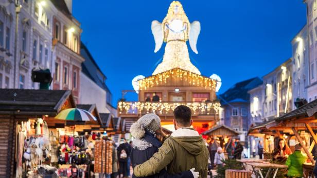 Paar steht in einem Weihnachtsdorf vor einem beleuchteten Engel