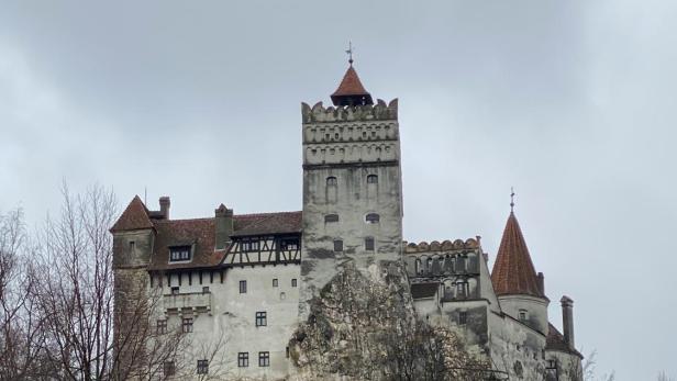 Schloss Bran in Siebenbürgen, das als „Draculas Schloss“ bekannt ist, erhebt sich auf einem Hügel vor bewölktem Himmel.