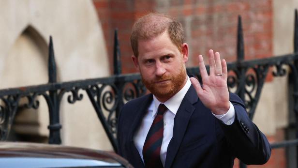 Prinz Harry winkt in einem dunklen Anzug mit gestreifter Krawatte.