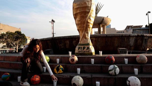 Frau in Guadalajara vor einem Monument mit WM-Pokal und Bällen zündet Kerzen an